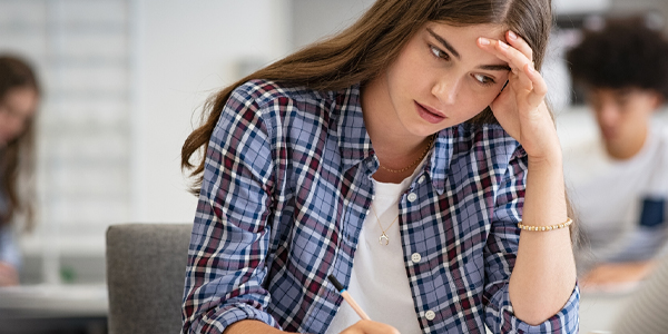 Menina sentada com a mão na cabeça demostra estresse na adolescência e o Colégio Alternativo ajuda nesse sentido. 