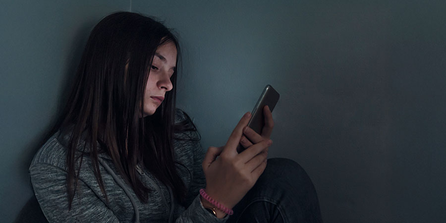 menina vendo celular com sinais que está sofrendo cyberbullying 