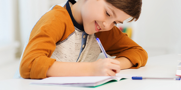 menino de cerca de 8 anos escrevendo com uma caneta e um caderno. Sorrindo.