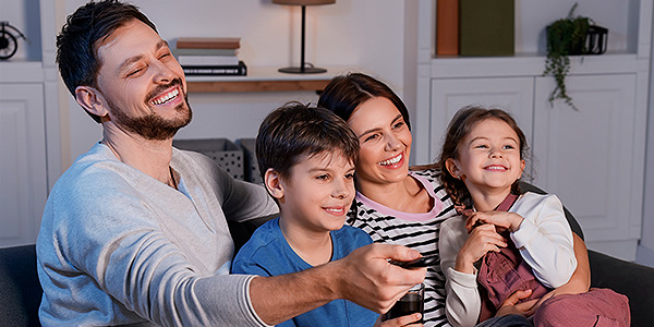 Pais e um casal de filhos pequenos com o controle remoto na mão para ver o filme Divertida Mente